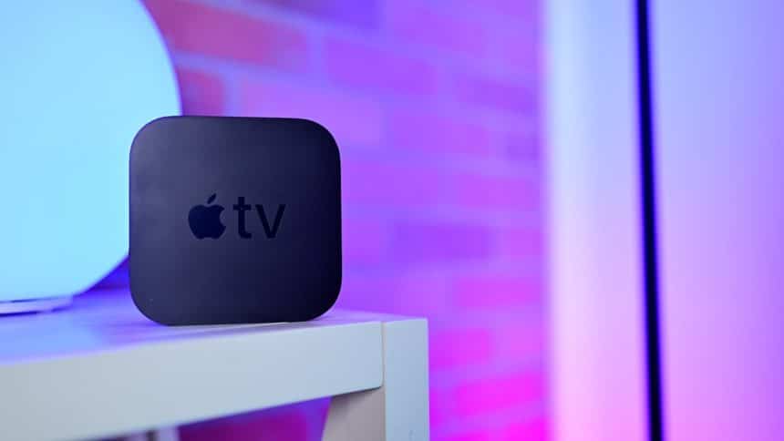 A black Apple TV device on a white shelf with purple lighting.