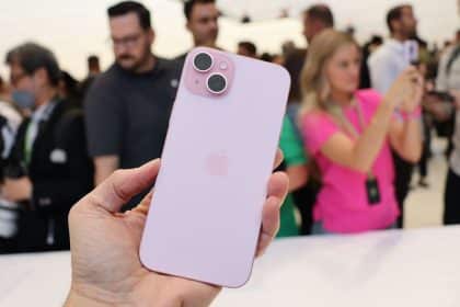 Person holding a pink iPhone 15 in a crowded event.