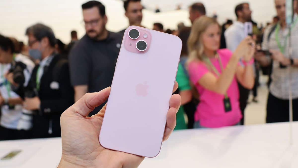 Person holding a pink iPhone 15 in a crowded event.