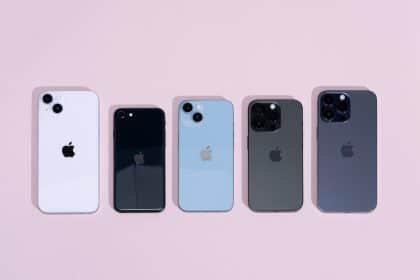 Five iPhone models in different colours displayed on a light pink background.