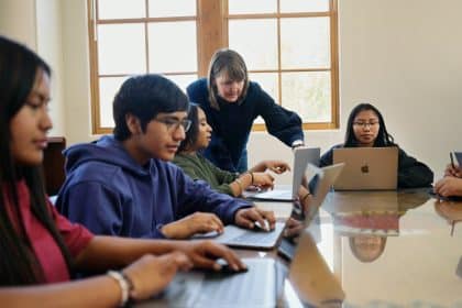 Teacher guiding students using laptops in a classroom setting.