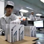 Factory worker handling iPhone packaging in a production facility.