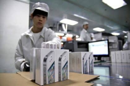 Factory worker handling iPhone packaging in a production facility.