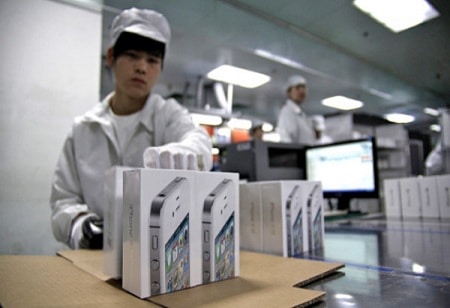 Factory worker handling iPhone packaging in a production facility.