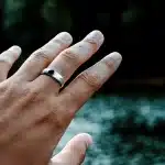 Hand wearing a smart ring near water.