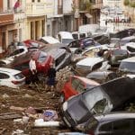 Flood damage with cars piled up and debris scattered in a Valencia street.