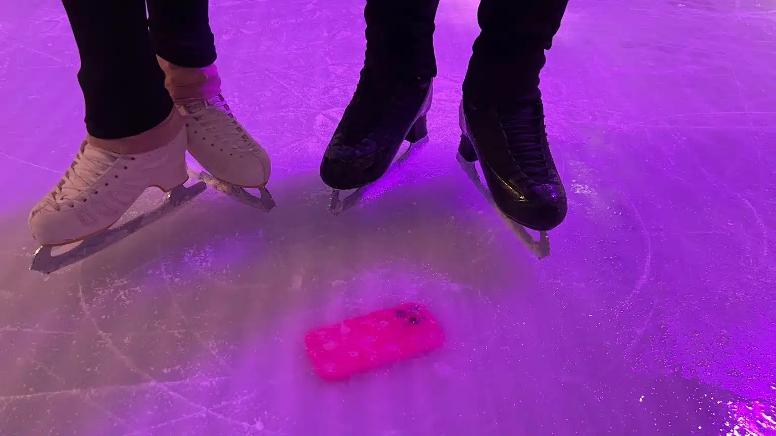 Skaters on ice with a pink iPhone frozen beneath the surface.