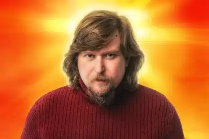 Man in red sweater with sunburst background.