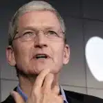 Apple CEO Tim Cook speaking at an event with the Apple logo in the background.