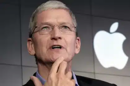 Apple CEO Tim Cook speaking at an event with the Apple logo in the background.