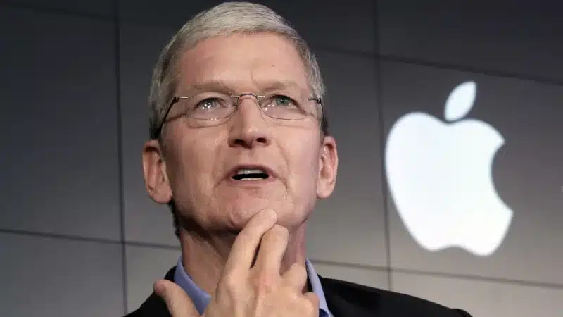 Apple CEO Tim Cook speaking at an event with the Apple logo in the background.