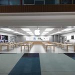 A modern Apple Store with glass walls, wooden tables, and Apple products on display.