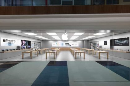 A modern Apple Store with glass walls, wooden tables, and Apple products on display.