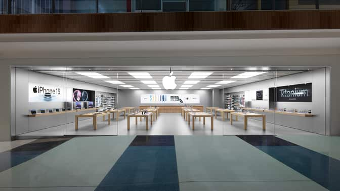 A modern Apple Store with glass walls, wooden tables, and Apple products on display.