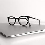 Black-framed glasses resting on a closed silver laptop