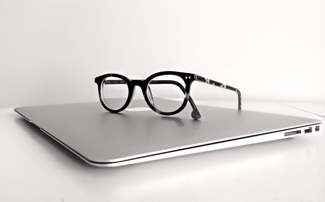 Black-framed glasses resting on a closed silver laptop