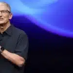 Tim Cook speaking on stage with a blue-lit background.