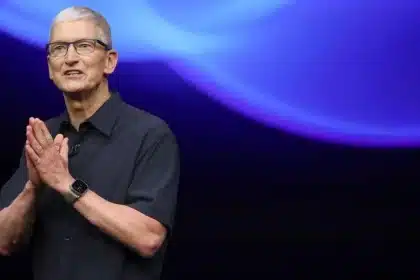 Tim Cook speaking on stage with a blue-lit background.