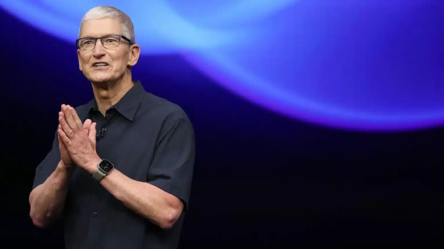 Tim Cook speaking on stage with a blue-lit background.