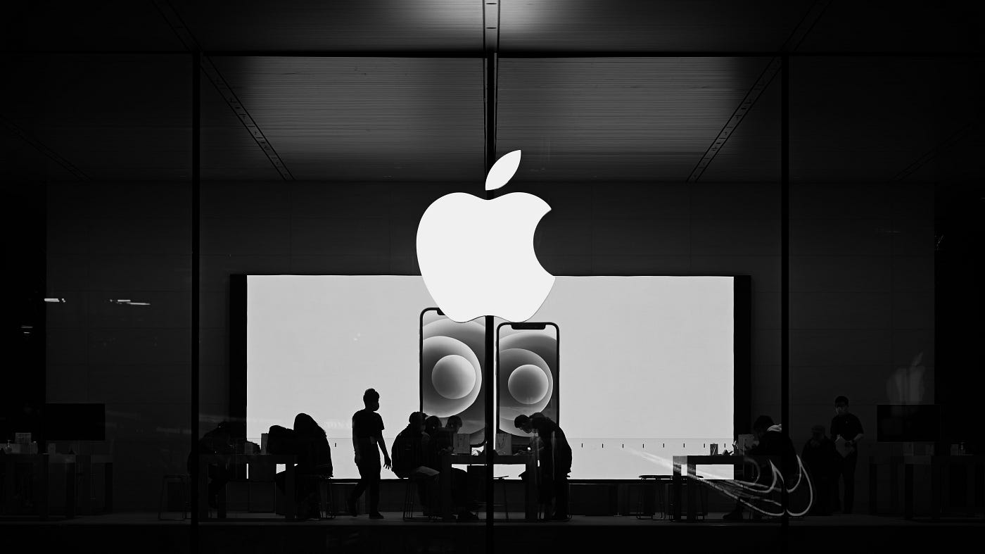 Apple Store with illuminated logo and customers inside.