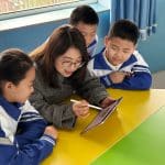 Teacher using a tablet to teach three young students in a classroom.