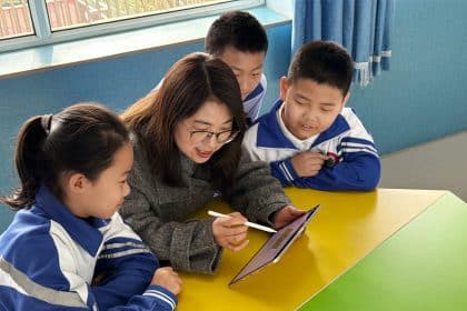 Teacher using a tablet to teach three young students in a classroom.