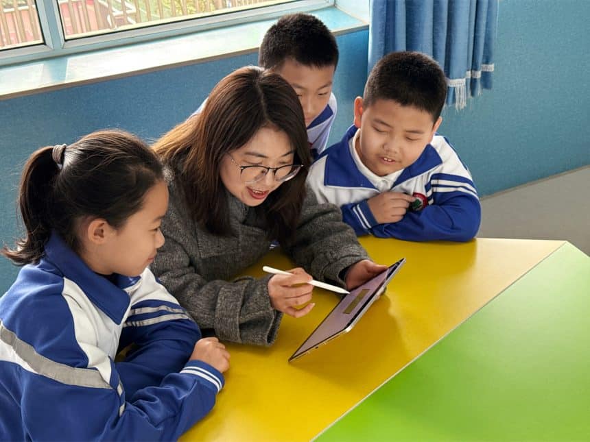 Teacher using a tablet to teach three young students in a classroom.