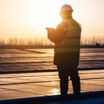 Engineer inspecting solar panels at sunset on a renewable energy site.