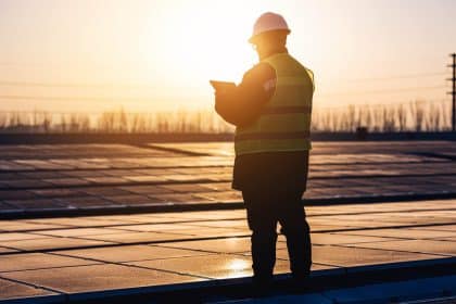 Engineer inspecting solar panels at sunset on a renewable energy site.